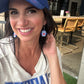 Woman wearing a blue cap and 'Buffalo' shirt, holding earrings with a casual outdoor setting.